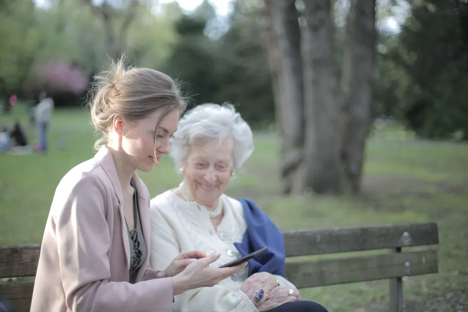 Une jeune femme et une femme âgée regardent un téléphone sur un banc de parc