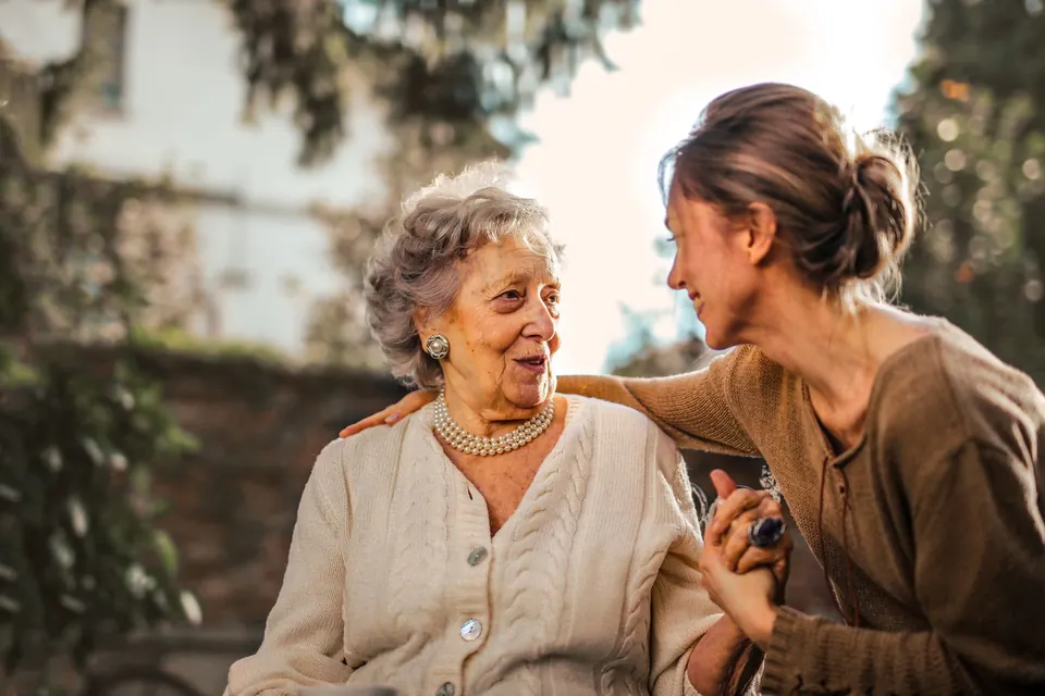 Une femme âgée et une femme plus jeune discutent dehors, main dans la main