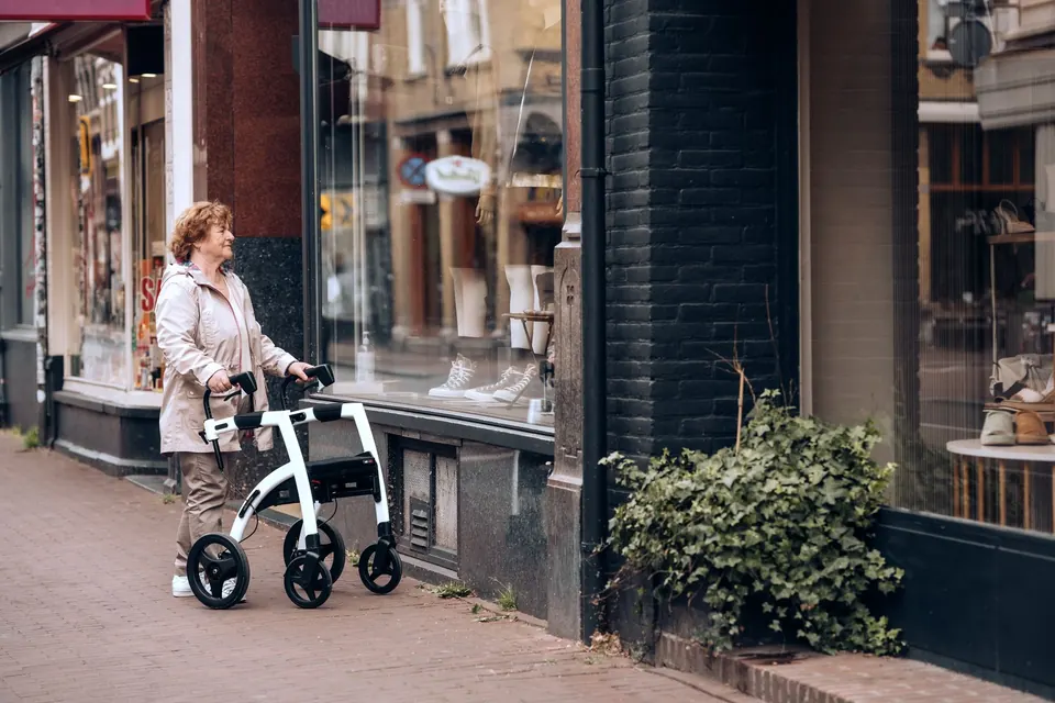 Une femme âgée avec un déambulateur à roulettes devant des vitrines