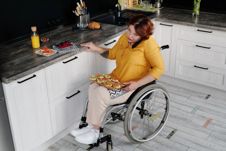 Une femme en fauteuil roulant prépare un plateau dans sa cuisine