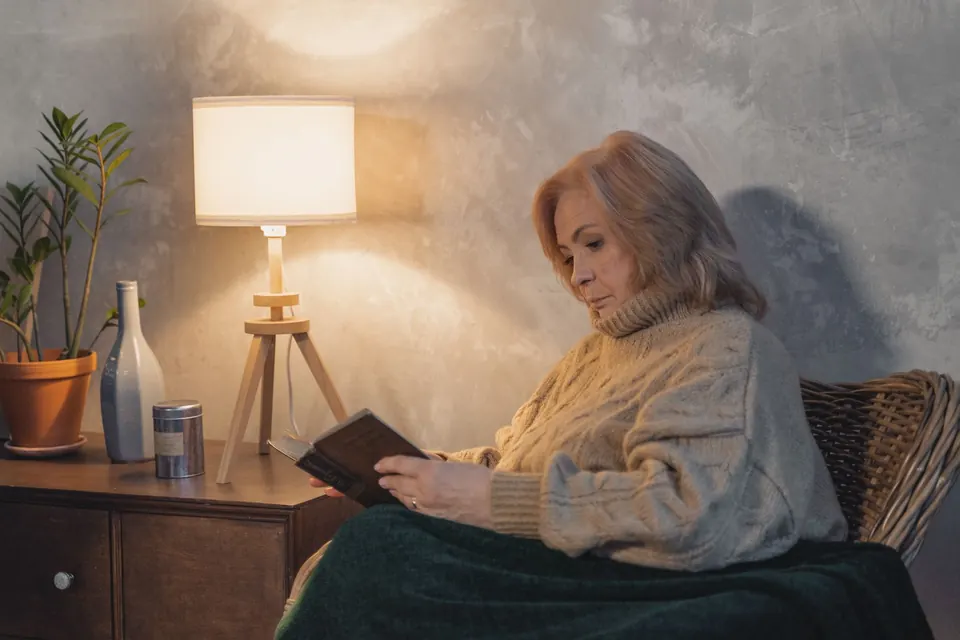 Une femme âgée lit dans un fauteuil, à la lumière d'une lampe